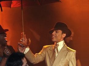 Someone smiling at Prince dressed in a gold metallic suit and carrying an umbrella