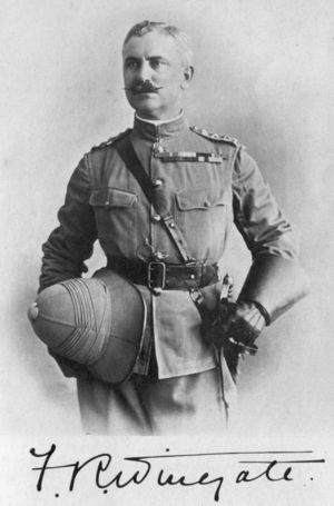 Mustached man in officers uniform. With San-Browne belt, sword at waist, wearing gauntlets and holding his pith helmet at waist level in his right hand.