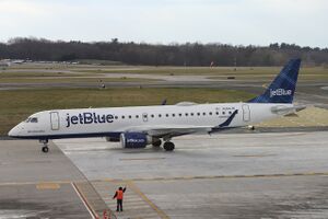 A white plane with the words "jetBlue" painted on the front and a blue tailfin taxies at an airport