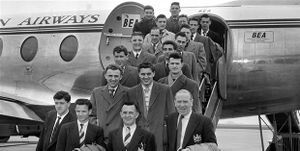 A black-and-white photograph of several people in suits and overcoats on the steps of an aircraft.