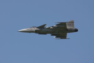 Slight underside view of jet aircraft flying perpendicular to the camera, against blue sky