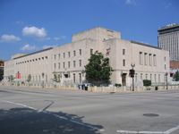 Exterior view of a gray building at a street corner. A separate, taller structure is visible in the background.