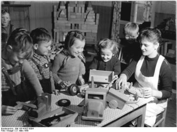 Four kindergarten children play with toy trucks on a table and a teacher sits with them while they play