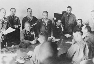 Nine Japanese officers sit across from three British officers at a table