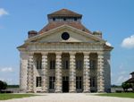 A large neo-classical white stone building, the triangular pediment is supported by six rough pillars.