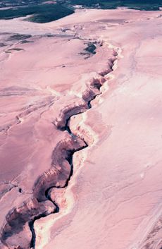 A thin stream winds through a thick layer of white, volcanic ash.