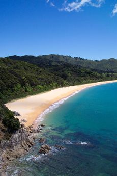 Photo showing clear blue water, a golden sanded beach and forested hills