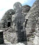 Three beehive shaped dry-stone huts surround a worn statue or cross