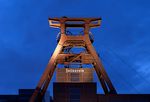 A orange metal tower with several flywheels above a building with Zollverein written in golden gothic script letters.