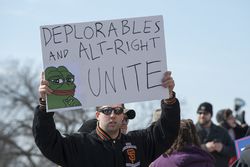 A man holds up a sign saying "DEPLORABLES AND ALT-RIGHT UNITE" with a cartoon frog in the corner.
