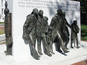 Bronze sculptures of seven figures marching stand around a large rectangular block of white engraved granite.