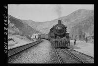 An American train transporting aid bound for the USSR stopping at a station. Supplies moved by road, rail and air through the Persian Corridor. c. 1943