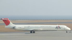 A McDonnell Douglas MD-81 aircraft taxiing on the tarmac, with a grey looking seaview on the background