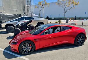A stainless steel clad ATV between a Tesla Cybertruck and a second generation Tesla Roadster in a parking lot during a Tesla event in 2020.