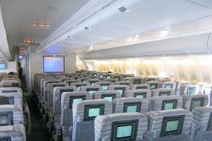 Inside view of an aircraft's Economy Class cabin with television on the back of the seats and overhead lockers on the ceiling