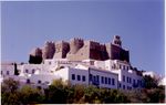 Fortress of dark stones on a hill above a town with white houses.