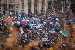Dozens of blue and yellow Ukrainian flags are held aloft in a wide crowd.
