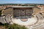 A mostly intact Roman amphitheater with a large wall behind the stage.