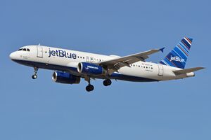 A white plane with the word "jetBlue" painted in the front and a blue tailfin on the back prepares to land as its landing gear is deployed