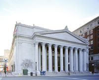 Exterior view of the front of a large, white building with ten pillars, and a set of stairs.