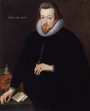 A portrait of Robert Cecil, who is standing at a table wearing black robes. He has neck length brown hair, and a pointed goatee. He has gold lettering behind him, which reads "sero, sed serio."