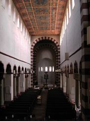 The interior of another long narrow church with high windows. The arch leading into the chancel at the far end has alternating red and white stones.