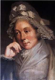 Quarter-length portrait of a woman in a brown and gray lace bonnet adorned with a bow and leaning on her right hand.