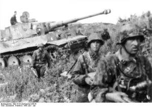 A medium field gray German tank advancing through a field surrounded by German soldiers in field gray uniforms.