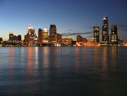 Tall buildings with city lights at dusk, reflected over still dark water