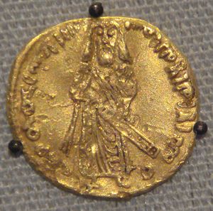 Obverse of golden coin depicting a standing, robed and bearded figure holding a long object, with Arabic inscriptions along the coin's rim