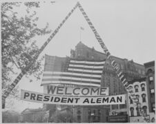 صورة لعلم الولايات المتحدة ولافتة الترحيب معلقة فوق أحد شوارع واشنطن خلال الاحتفالات على شرف الرئيس الزائر ميگيل أليمان فالديس.