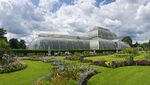 A large greenhouse with rounded ends and sides sits in the middle of groomed grass and flower beds.