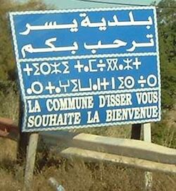 لافتة ترحيب بثلاث لغات في يسر، مكتوبة بالعربية, بالقبيلي (Tifinagh script)، وبالفرنسية. ("بلدية يسر ترحب بكم.")